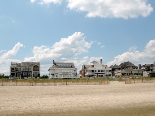 A row of beach houses along a sandy shore under a blue sky with fluffy clouds.