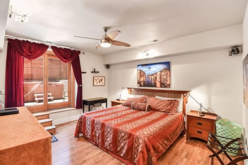 Cozy bedroom with a large bed, wooden floors, red curtains, and a view of a patio through sliding glass doors.