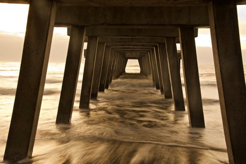 View of a pier's support beams with waves gently lapping underneath, creating a serene coastal scene.