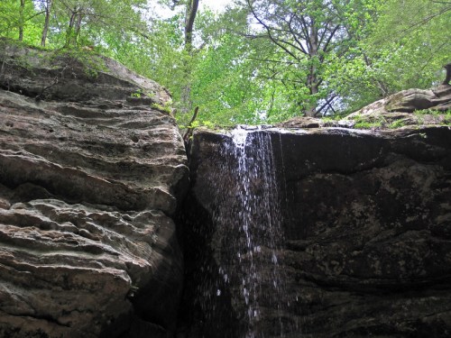 A waterfall cascading over rocky cliffs, surrounded by lush green trees and foliage.