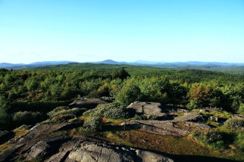 A panoramic view of lush green hills and rocky terrain under a clear blue sky.