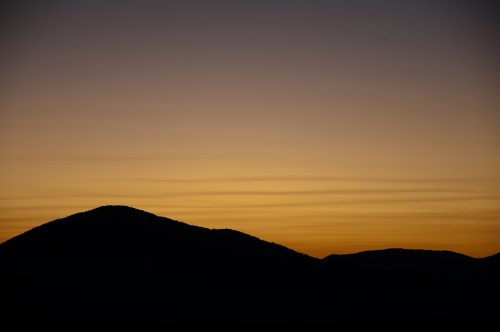 Silhouetted mountains against a gradient sunset sky, transitioning from deep blue to warm orange hues.