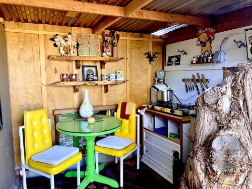 A cozy kitchen with yellow chairs, a green table, wooden shelves, and various kitchen items on display.