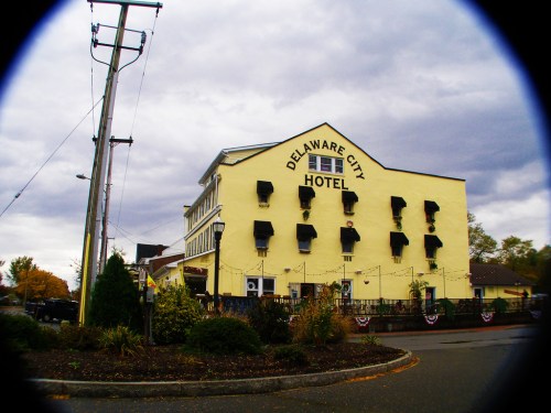 A yellow hotel building with black window awnings, surrounded by greenery and a cloudy sky.