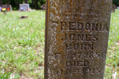 Close-up of a weathered gravestone inscribed with "Fredonia Jones, Born 1846, Died 1915," surrounded by grass.