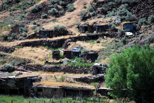 Abandoned structures on a hillside, surrounded by dry grass and sparse vegetation.