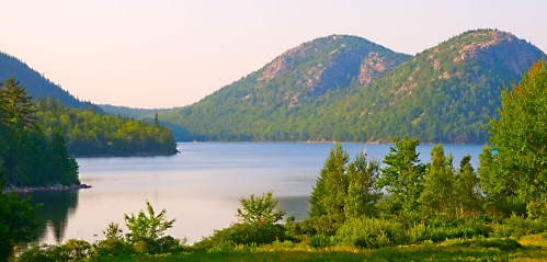 Serene landscape featuring a calm lake surrounded by lush greenery and rolling hills under a soft, pastel sky.