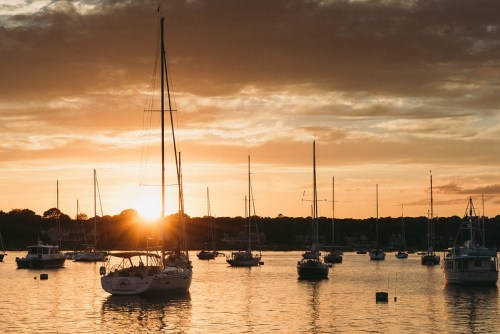 Sailboats anchored in a calm harbor at sunset, with warm golden light reflecting on the water.