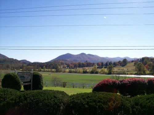 Scenic view of rolling hills and mountains under a clear blue sky, with green fields and shrubs in the foreground.