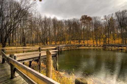 A serene pond surrounded by bare trees and autumn foliage, with a wooden walkway extending over the water.