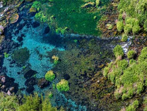 Aerial view of a clear, turquoise river with rocks and lush green vegetation along the banks.