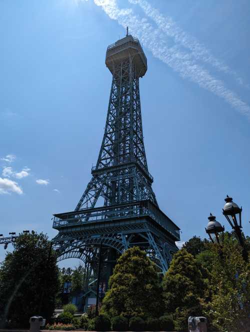 A tall, blue steel tower resembling the Eiffel Tower, surrounded by trees and a clear blue sky.