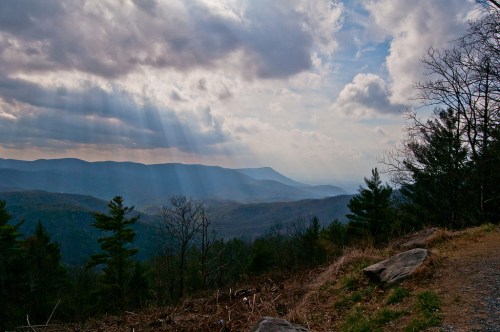 A scenic view of mountains under a cloudy sky, with rays of sunlight breaking through the clouds.
