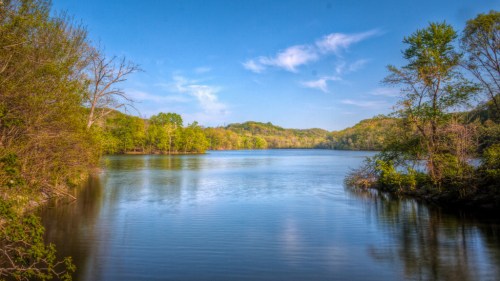 A serene lake surrounded by lush greenery and rolling hills under a clear blue sky.