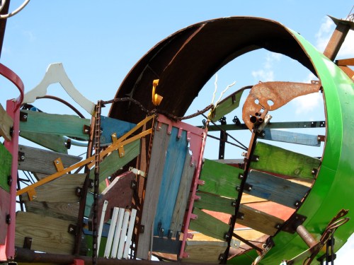 Colorful abstract sculpture made of various materials, featuring curved and angular shapes against a blue sky.