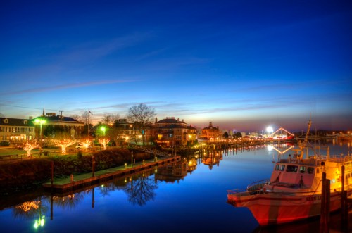 A serene waterfront scene at dusk, featuring a boat, colorful lights, and reflections on calm water.