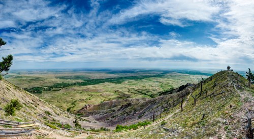 Panoramic view of rolling green hills under a blue sky with scattered clouds, showcasing a vast, open landscape.