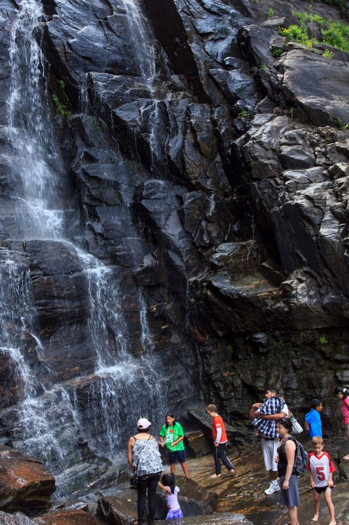 A group of people, including children, explore a rocky area near a waterfall, enjoying the natural scenery.