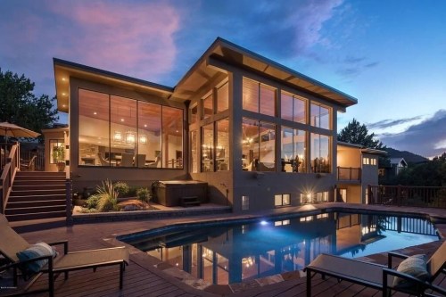 Modern house with large windows, pool, and outdoor seating, set against a twilight sky.
