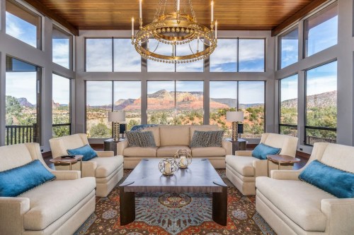Bright living room with large windows showcasing mountain views, featuring a chandelier, cozy seating, and decorative accents.