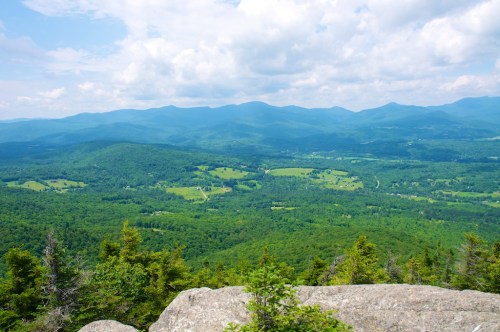 A panoramic view of lush green mountains and valleys under a partly cloudy sky.