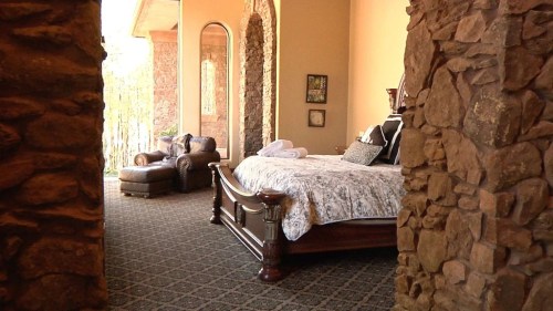 Cozy bedroom with a large bed, decorative pillows, and a stone archway, featuring a lounge chair and natural light.