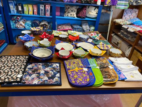 A display of colorful bowls, tableware, and kitchen textiles on a wooden table in a shop.