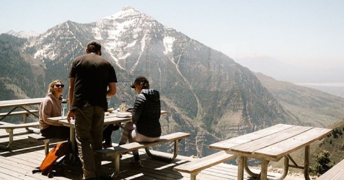 A group of people enjoying a meal at a picnic table with a stunning mountain view in the background.