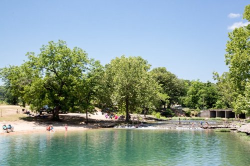 A serene lake surrounded by trees, with people relaxing on the shore and enjoying the sunny day.