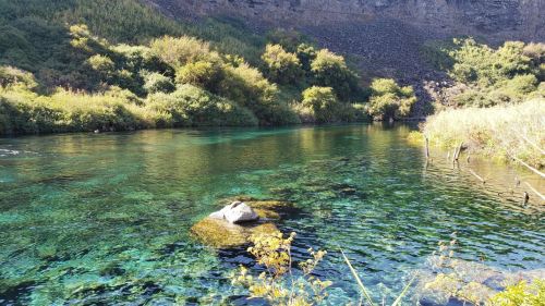 A serene river scene with clear turquoise water, surrounded by lush greenery and rocky terrain.