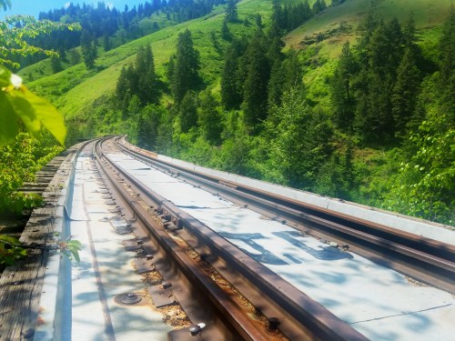 A winding railway track surrounded by lush green hills and trees under a clear blue sky.