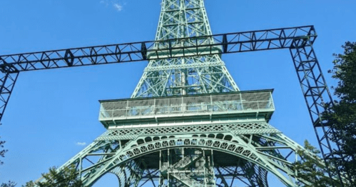 View of the Eiffel Tower from below, framed by a clear blue sky and greenery.