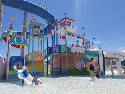 A colorful water park with slides and children playing in the water under a clear blue sky.