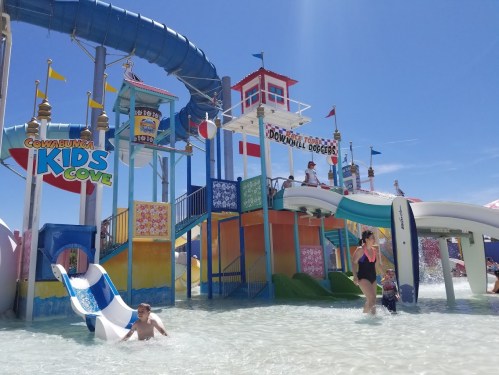 A colorful water park with slides and children playing in the water under a clear blue sky.