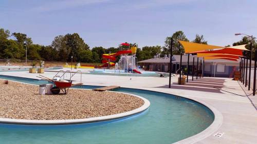 A sunny water park featuring a winding pool, colorful slides, and shaded areas with lounge chairs.