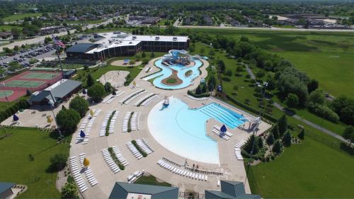 Aerial view of a large water park with pools, slides, and lounge chairs, surrounded by green fields and buildings.