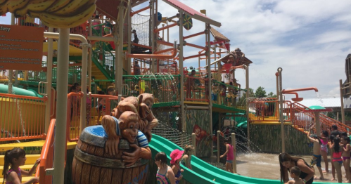 A vibrant water park with slides, play structures, and children enjoying the water on a sunny day.