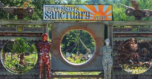 Colorful entrance to Three Sisters Sanctuary, featuring artistic sculptures and a bright sun design above the archway.