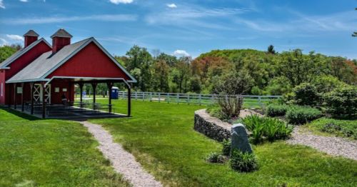 A red barn with a path leading to it, surrounded by green grass and trees under a blue sky.