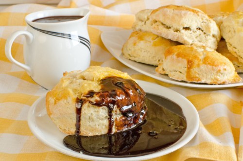 A plate of freshly baked biscuits drizzled with chocolate sauce, alongside a cup of coffee on a checkered tablecloth.