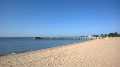 A serene beach scene featuring a wooden pier extending into calm waters under a clear blue sky.