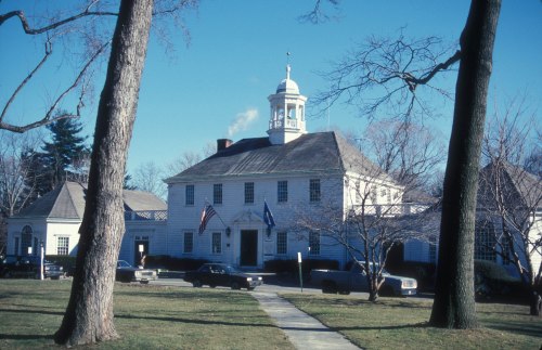 Historic building with a cupola, flanked by trees, featuring American flags and a clear blue sky.