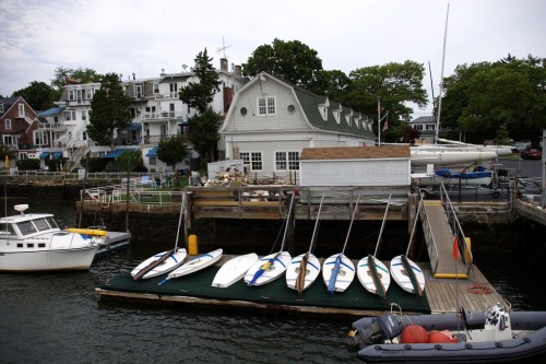 A marina with several boats docked, including kayaks and a small white boat, near a waterfront building.