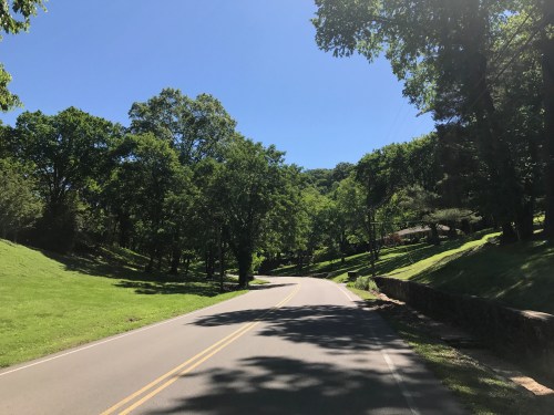 A scenic road lined with lush green trees under a clear blue sky.