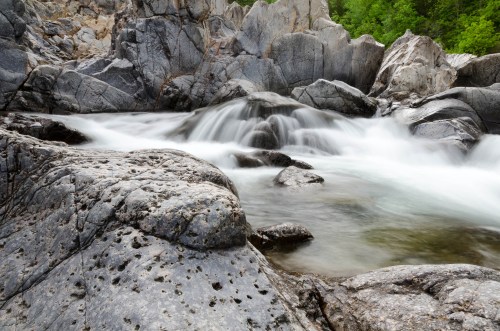 A serene river flows over smooth rocks, surrounded by rugged cliffs and lush greenery.