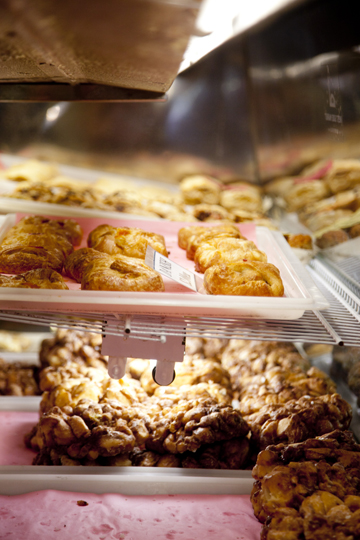 A display case filled with various pastries, including croissants and nut-covered treats, on a pink tray.