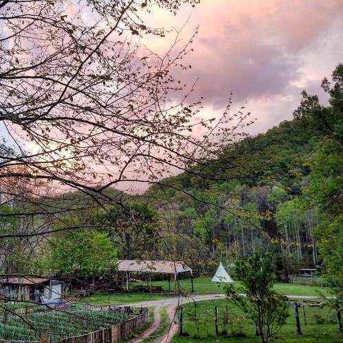 A serene landscape featuring a path leading to a rustic cabin and a teepee, with a colorful sunset sky above.