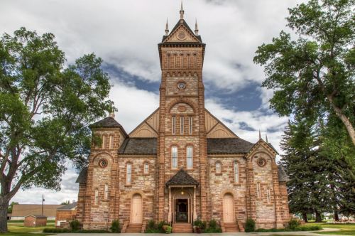 Historic stone church with a tall clock tower, surrounded by trees and a cloudy sky.
