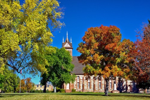 A historic building surrounded by vibrant autumn trees in shades of yellow, orange, and green under a clear blue sky.