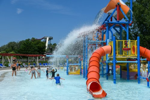 Children play in a water park with colorful slides and splash features under a clear blue sky.